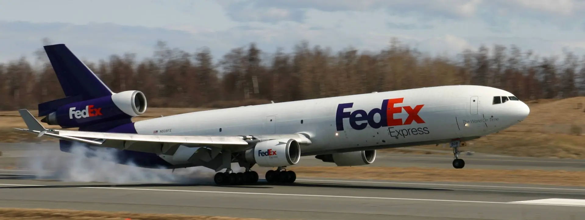Podwozie główne samolotu FedEx MD-11 styka się z pasem startowym. Zdjęcie zrobione w pogodny dzień na początku maja 2008 roku na międzynarodowym lotnisku Teda Stevensa w Anchorage na Alasce.